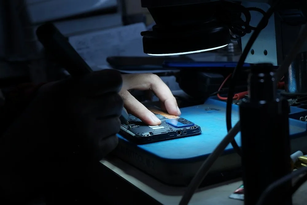 A gloved LaptopHaber engineer working on a circuit board under task lighting at the component-level repair station