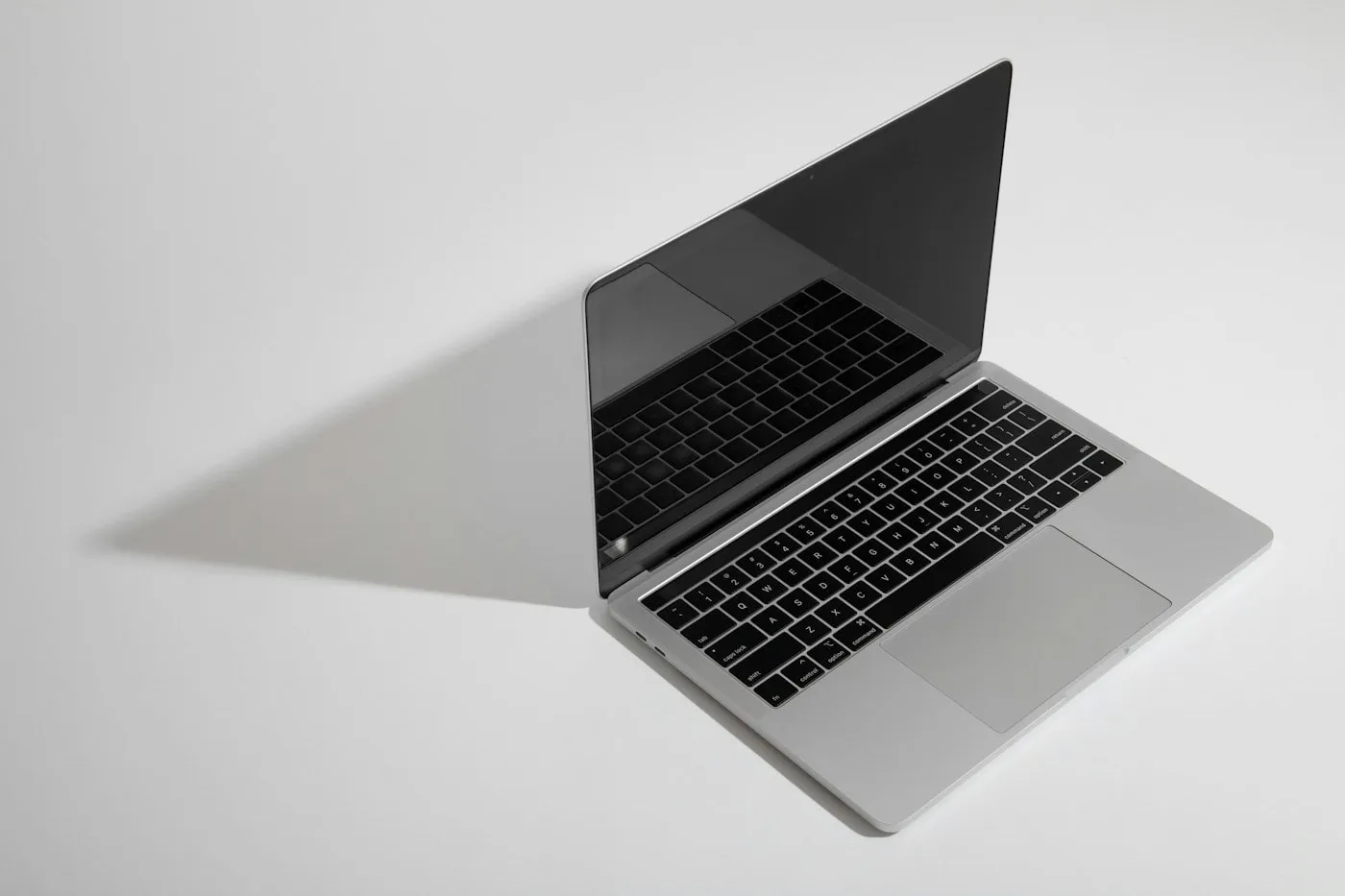 A silver laptop open on a plain white surface, lit from the side