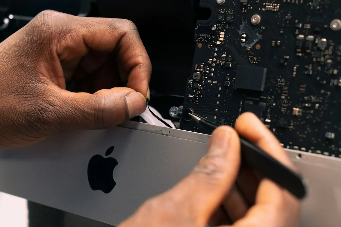 A technician carefully lifting the bottom cover away from a laptop during a teardown